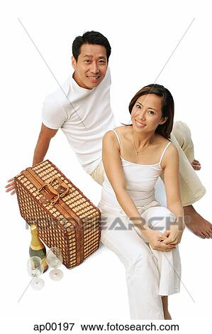 Stock Photo - Couple sitting on floor with picnic basket, wine bottle and glasses. Fotosearch