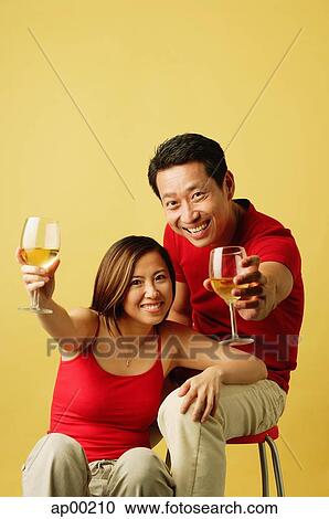 Couple sitting, raising drinks towards camera View Large Photo Image Stock Image - Couple sitting, raising drinks towards camera. Fotosearch