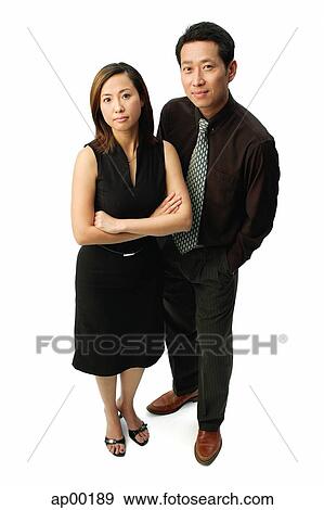 Stock Photo - Couple standing, looking at camera, woman with arms crossed. Fotosearch