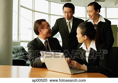 Stock Image - Executives having a discussion in office, laptop open on table. Fotosearch
