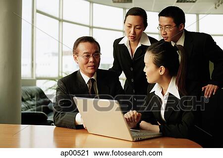 Stock Image - Executives in office, having a meeting, laptop open in front of them. Fotosearch