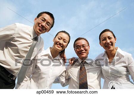 Stock Photo - Executives looking down at camera, arms around each other, smiling. Fotosearch
