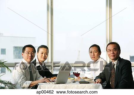 Stock Image - Executives sitting at lunch table, looking at camera. Fotosearch