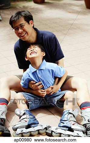 Stock Image - Father and son sitting, looking at camera. Fotosearch