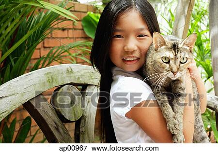 Stock Photo - Girl holding cat, looking at camera, smiling. Fotosearch
