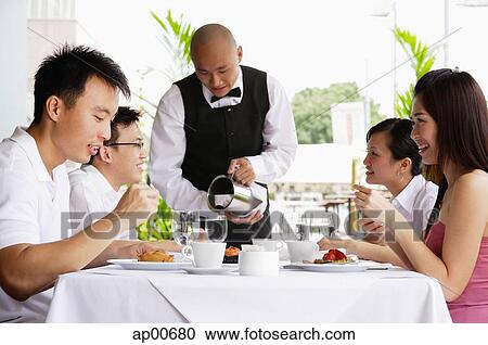 Group of friends at restaurant eating, waiter pouring water at their table View Large Photo Image Stock Image - Group of friends at restaurant eating, waiter pouring water at their table. Fotosearch