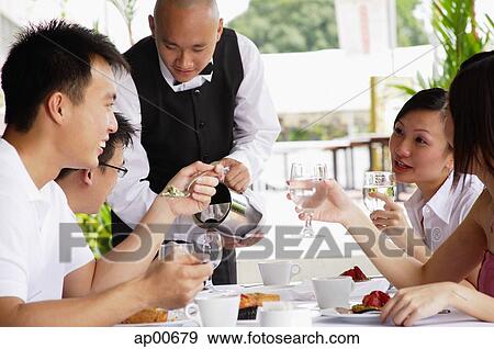 Group of friends having lunch, waiter pouring water at their table View Large Photo Image Stock Photo - Group of friends having lunch, waiter pouring water at their table. Fotosearch