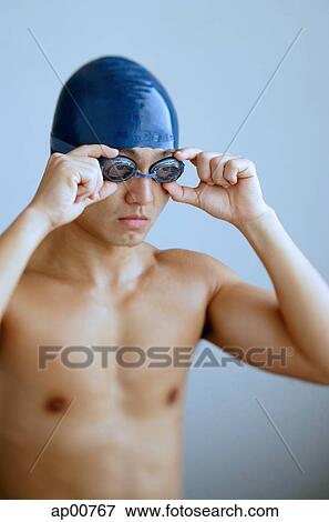 Stock Photo - Man adjusting goggles, wearing swimming cap. Fotosearch