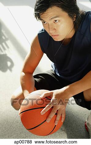 Stock Photo - Man crouching, holding basketball, portrait. Fotosearch