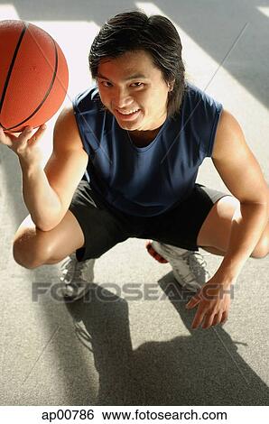 Stock Photograph - Man crouching, holding basketball, looking up at camera. Fotosearch