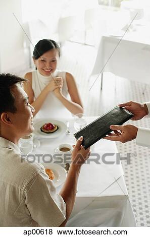Stock Photo - Man giving menu to waiter, woman sitting opposite him. Fotosearch