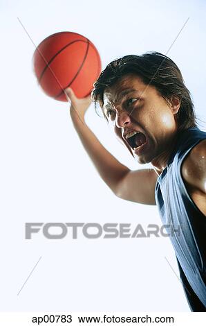 Stock Image - Man holding basketball in the air, mouth open. Fotosearch