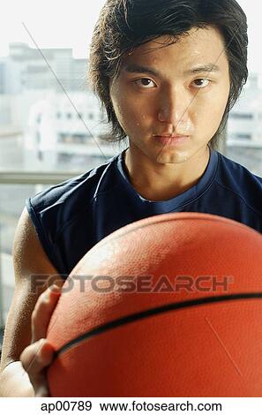 Stock Photo - Man holding basketball, looking at camera. Fotosearch