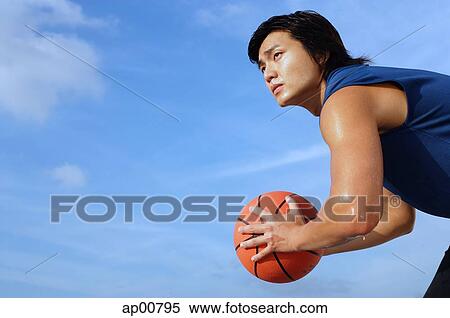 Stock Photography - Man holding basketball, looking away, side view. Fotosearch