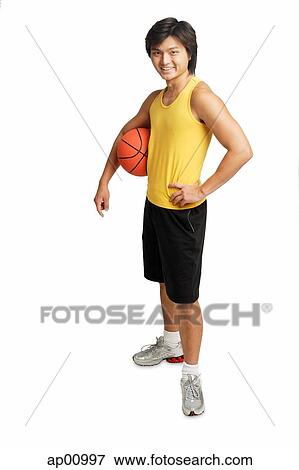 Stock Photo - Man holding basketball under arm, hand on hip, looking at camera. Fotosearch