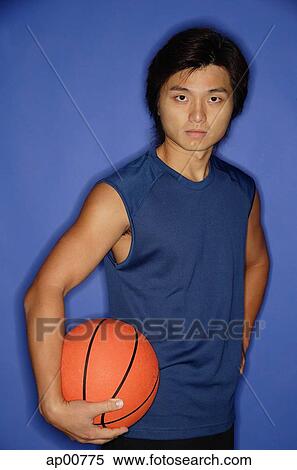 Stock Photography - Man holding basketball under arm, looking at camera. Fotosearch