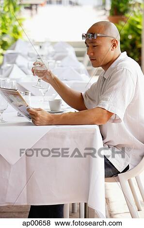Man sitting at table, reading newspaper, holding glass of water View Large Photo Image Stock Photo - Man sitting at table, reading newspaper, holding glass of water. Fotosearch