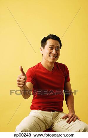 Stock Photo - Man sitting, looking at camera, making thumbs up sign. Fotosearch