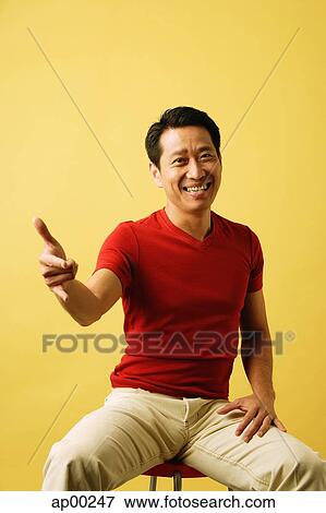 Man sitting, looking at camera, pointing finger View Large Photo Image Stock Photo - Man sitting, looking at camera, pointing finger. Fotosearch