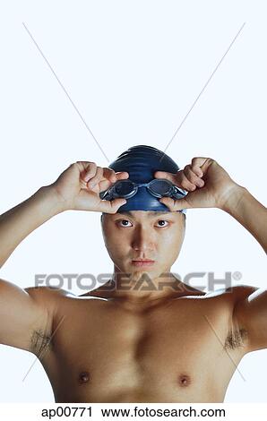 Stock Image - Man touching swimming goggles, looking at camera, portrait. Fotosearch