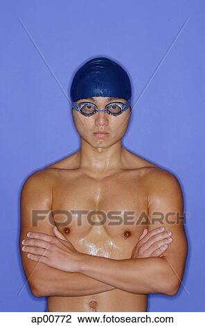 Stock Image - Man wearing swimming cap and goggles, arms crossed, portrait. Fotosearch