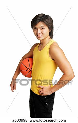 Stock Photo - Man with basketball under arm, hand on hip, looking at camera. Fotosearch
