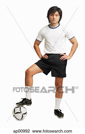 Stock Image - Man with hands on hips, one leg on soccer ball. Fotosearch