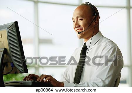 Man with headset, using desktop PC, smiling View Large Photo Image Picture - Man with headset, using desktop PC, smiling. Fotosearch