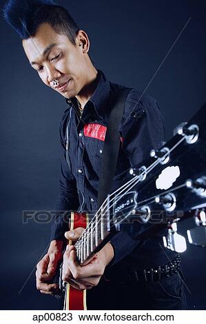 Stock Image - Man with mohawk, holding guitar, looking down. Fotosearch