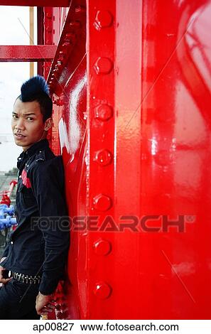 Stock Photo - Man with mohawk, leaning on wall, looking at camera. Fotosearch