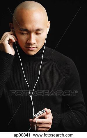 Stock Image - Man with shaved head, listening to music with earphones. Fotosearch