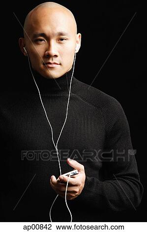 Man with shaved head, listening to music with earphones, looking at camera View Large Photo Image Stock Image - Man with shaved head, listening to music with earphones, looking at camera. Fotosearch