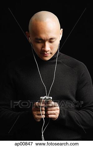 Stock Photo - Man with shaved head, listening to music with earphones. Fotosearch