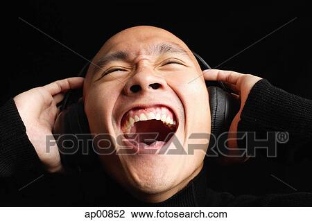 Stock Image - Man with shaved head, wearing headphones, mouth open. Fotosearch