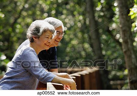 Stock Image - Mature couple leaning on railing, smiling, looking away. Fotosearch