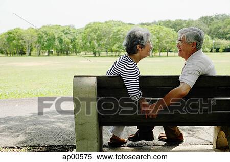 Stock Photography - Mature couple sitting face to face on park bench, holding hands. Fotosearch