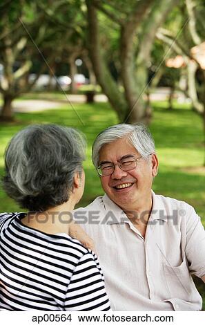 Picture - Mature couple sitting in park, facing each other, man smiling. Fotosearch