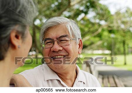 Stock Photography - Mature couple sitting in park, facing each other, man smiling. Fotosearch
