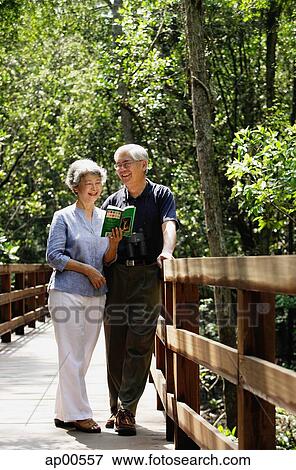 Mature couple standing side by side, talking, woman looking at book View Large Photo Image Stock Photo - Mature couple standing side by side, talking, woman looking at book. Fotosearch
