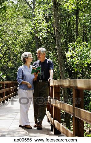 Mature couple standing side by side, talking, woman holding book View Large Photo Image Stock Photograph - Mature couple standing side by side, talking, woman holding book. Fotosearch