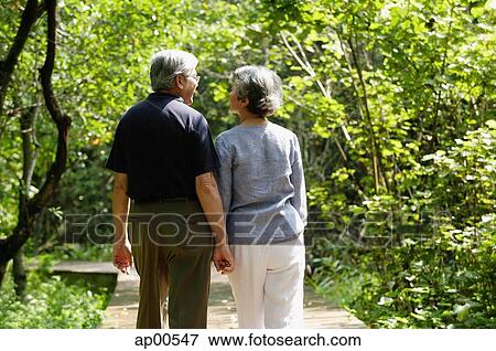Stock Photo - Mature couple walking through park, holding hands, rear view. Fotosearch
