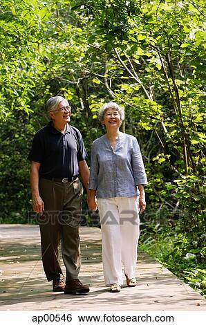 Stock Photograph - Mature couple walking through park, holding hands, smiling. Fotosearch