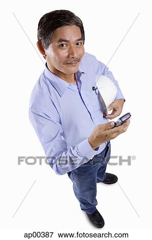 Mature man holding construction hat, using mobile phone, looking at camera View Large Photo Image Stock Photo - Mature man holding construction hat, using mobile phone, looking at camera. Fotosearch
