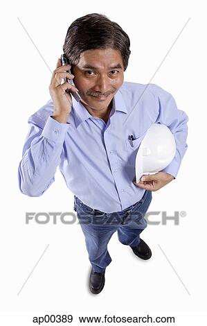 Mature man holding construction hat, using mobile phone, looking at camera View Large Photo Image Stock Photo - Mature man holding construction hat, using mobile phone, looking at camera. Fotosearch