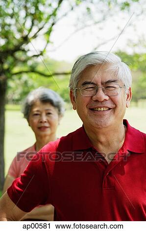 Stock Image - Mature man, looking at camera, woman standing behind him. Fotosearch
