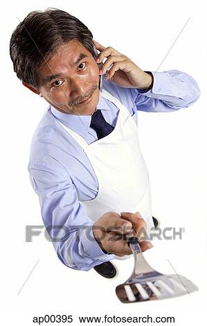 Mature man wearing apron, using mobile phone, holding spatula towards camera View Large Photo Image Stock Photography - Mature man wearing apron, using mobile phone, holding spatula towards camera. Fotosearch