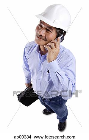 Mature man wearing construction hat, using mobile phone, looking away View Large Photo Image Picture - Mature man wearing construction hat, using mobile phone, looking away. Fotosearch