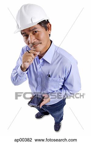 Stock Image - Mature man wearing construction hat, holding PDA, hand on chin, looking at camera. Fotosearch