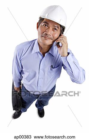 Stock Image - Mature man wearing construction hat, using mobile phone. Fotosearch