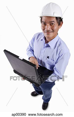 Mature man wearing construction hat, holding laptop, portrait View Large Photo Image Stock Image - Mature man wearing construction hat, holding laptop, portrait. Fotosearch